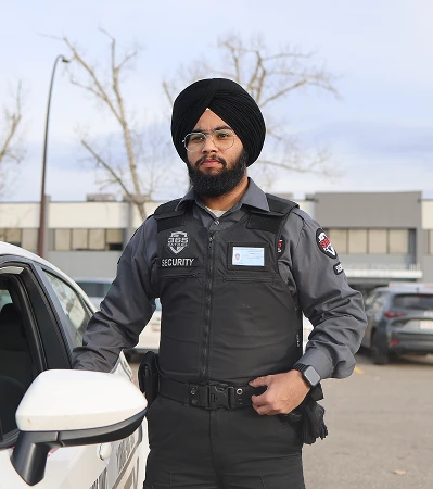 A uniformed security guard standing next to a patrol car, representing the professional team behind our Calgary Security Services & Edmonton Patrols.