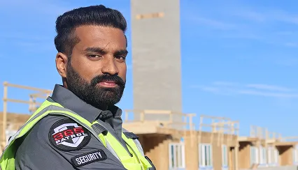 A uniformed security guard in a high-visibility vest standing in front of a residential development, illustrating our construction Calgary security service capabilities.